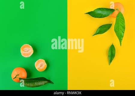 Mature di mandarini con foglie di colore giallo e lo sfondo di colore verde per il progetto. Vista dall'alto. Spazio di copia Foto Stock