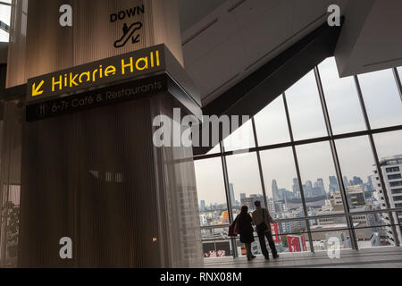 Una donna e un uomo giapponesi guardano fuori una vista di Shinjuku dalle grandi finestre nella torre dell'Hikarie a Shibuya, Tokyo, Giappone. Foto Stock