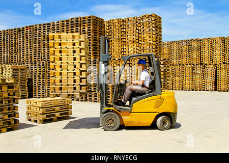 L'operatore del carrello di movimentazione pallet di legno in magazzino Foto Stock