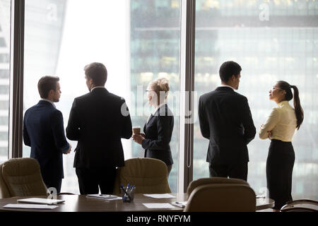 Vista posteriore dei dirigenti internazionali team parlando vicino alla finestra di ufficio Foto Stock