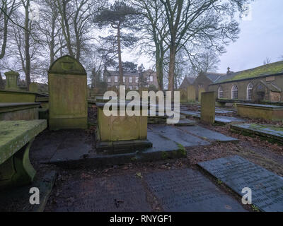 Haworth chiesa cimitero, West Yorkshire, con il Bronte Parsonage Museum e Old schoolhouse in background, all'inizio di mattina nebbia in inverno Foto Stock