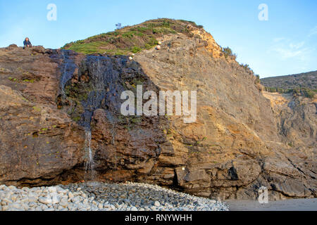 Escursionista sat sulla cima di scogliere di granito sulla spiaggia lungo la costa sud via Foto Stock
