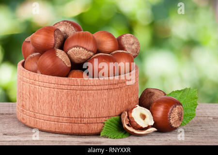 Le nocciole con foglie in una ciotola di legno su un tavolo in legno con giardino sfocata sullo sfondo. Foto Stock