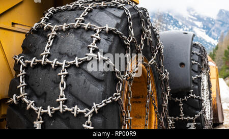 Il caricatore anteriore per la rimozione della neve con metallo di catene da neve a ruote. Rimozione della neve in montagna. Foto Stock