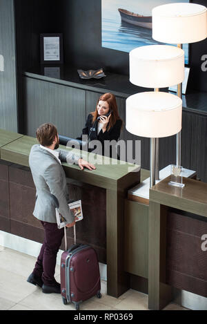 Receptionist femmina parlando al telefono mentre imprenditore permanente al contatore Foto Stock