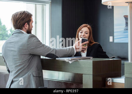 Imprenditore mostra smart phone al receptionist femmina Foto Stock