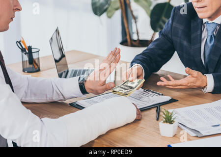 Vista ritagliata di lavoratore di rigetto di denaro dando businessman in giacca blu in ufficio, concetto di compensazione Foto Stock