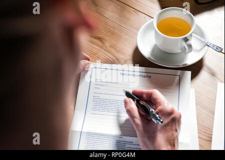 Frauenhaende die eine Patientenverfuegung ausfuellen auf einem Tisch mit einer Teetasse signor: sì PR: Sì Foto Stock