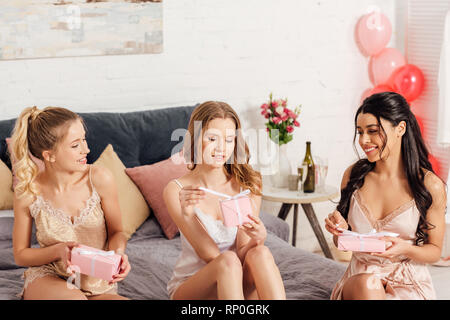 Bella sorridente ragazze multiculturale in apertura nightwear presenta durante il pigiama party Foto Stock