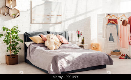 Design moderno degli interni di una camera da letto con orsacchiotto di peluche giocattoli, cuscini, piante e letto matrimoniale Foto Stock