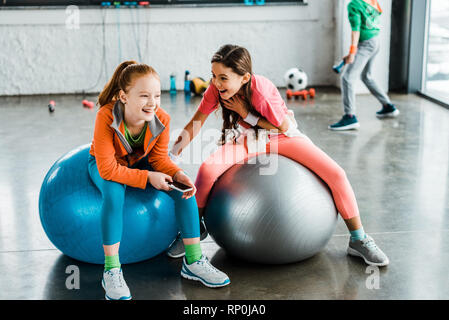 Ridere i bambini con lo smartphone seduti sulle sfere di fitness Foto Stock