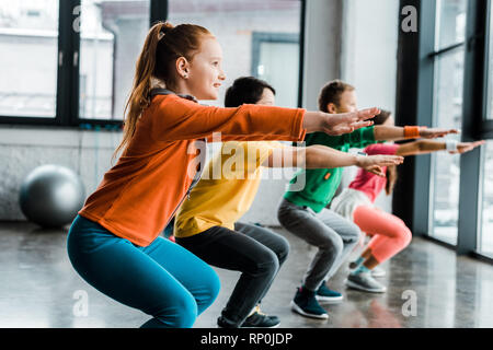 Concentrate i bambini facendo squat durante gli allenamenti in palestra Foto Stock