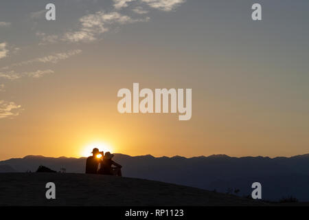 Un giovane seduto su di una duna di sabbia al tramonto stagliano contro il sole, Mesquite Flat dune di sabbia, il Parco Nazionale della Valle della Morte, California, Stati Uniti Foto Stock