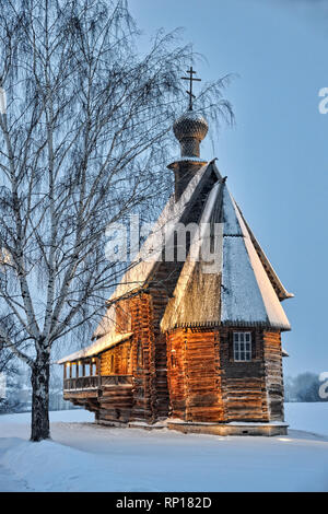 = vecchia chiesa di legno incorniciata da albero in inverno al crepuscolo = coperto neve vecchia chiesa in legno di San Nicola per motivi di Suzdal il Cremlino incorniciato da b Foto Stock
