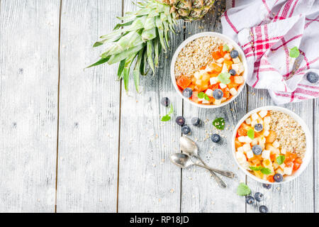 Sana colazione fiocchi d'avena con frutta tropicale e bacche, bianco su sfondo di legno spazio copia Foto Stock