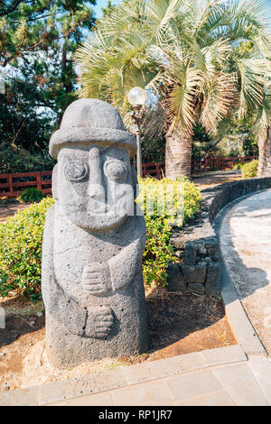 Dol hareubang nonno di pietra con alberi di palma tropicali a Daepo Jusangjeolli in Jeju Island, Corea Foto Stock