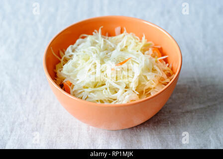 Primo piano della piccola orange ciotola riempita con cavolo fermentato e la carota sulla tavola bianco Foto Stock