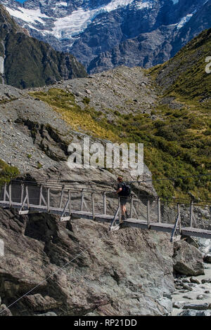 Donna passando una sospensione ponte su un fiume del ghiacciaio in Mount Cook area in Nuova Zelanda Foto Stock