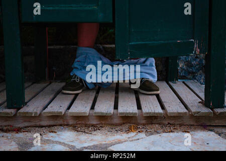 I piedi di un uomo che si siede nel WC. Pubblico wc in legno con tavole di legno sul fondo. Problemi Stomack concept Foto Stock