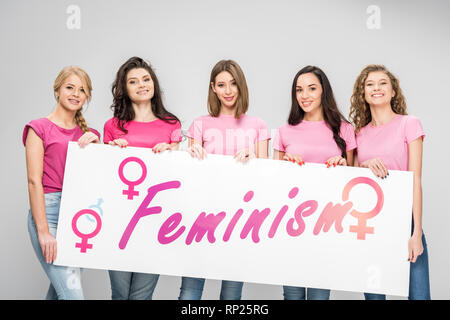 Allegro ragazze tenendo premuto segno di grandi dimensioni con il femminismo lettering isolato su grigio Foto Stock