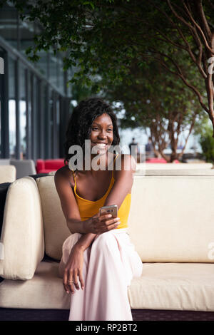 Un attraente ed elegante brasiliano africana donna seduta su una sedia a sdraio Foto Stock