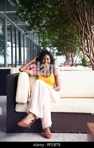 Un attraente ed elegante brasiliano africana donna seduta su una sedia a sdraio Foto Stock