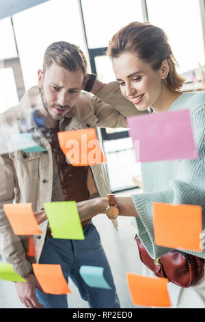 Casual uomo d affari e imprenditrice mettendo colorato sticky notes sul vetro della finestra in ufficio Foto Stock