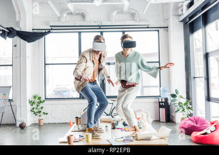 Maschi e femmine di architetti indossando le cuffie vr, gesti con le mani e aventi esperienza virtuale in ufficio loft Foto Stock