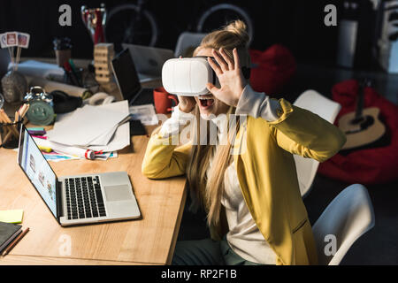 Emozionato casual imprenditrice gesti con le mani mentre avente esperienza virtuale al computer scrivania in ufficio Foto Stock