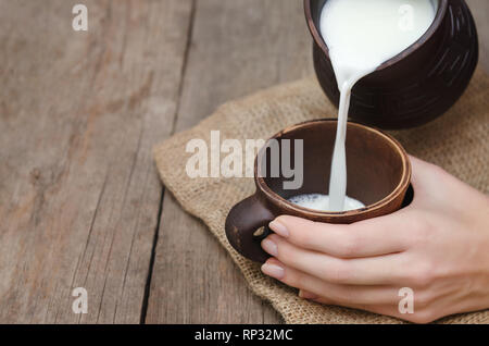 Latte fresco versando in una tazza di argilla su sfondo di legno. Foto Stock