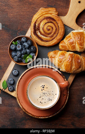Caffè, cornetti, panini alla cannella e le bacche di prima colazione. Sul tavolo di legno Foto Stock