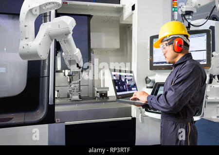 Tecnico di manutenzione utilizzando il computer portatile il controllo automatico di mano robotica con macchina CNC in smart factory, industria 4.0 concetto Foto Stock