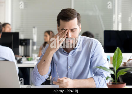 Lavoratore di ufficio seduti alla scrivania prendendo il largo bicchieri sfregamento occhio massaggiante stanco di lavorare al computer avente visione offuscata problema e occhi secchi dopo lo Foto Stock