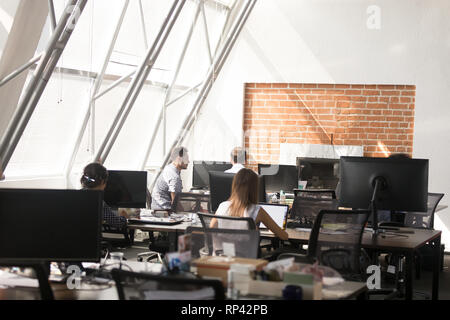 I dipendenti di sesso maschile di lavoro femminile in coworking spazio aperto avente workday occupato tramite computer seduto alla scrivania, posteriore vista posteriore. Gli studenti popolo millenario Foto Stock