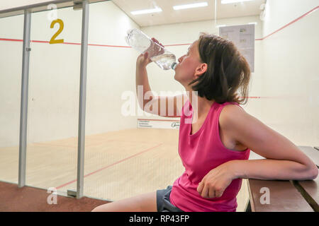 Una donna si prende una pausa dal giocare a squash e bevande a partire da una bottiglia di acqua per il ristoro Foto Stock