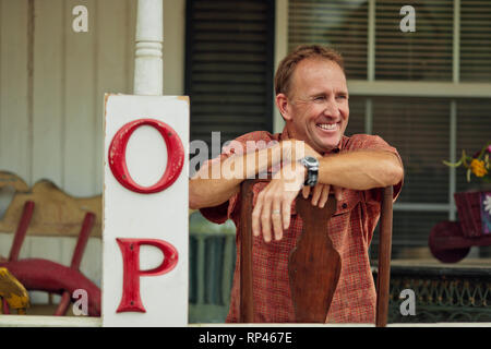 Sorridente maturare il proprietario del negozio si rilassa sulla veranda del suo negozio di antiquariato. Foto Stock