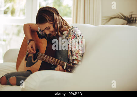 Sorridente ragazza giovane la riproduzione di musica su chitarra a casa. Ragazza adolescente di imparare a suonare la chitarra. Foto Stock