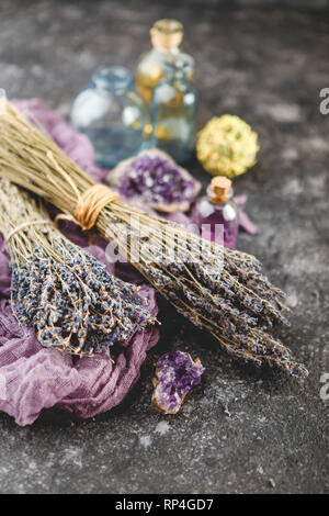 Mazzi di fiori di lavanda secchi, ametista druses e olio di lavanda in una piccola bottiglia sul baclground scuro. Medicina alternativa tema Foto Stock