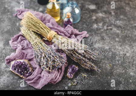 Mazzi di fiori di lavanda secchi, ametista druses e olio di lavanda in una piccola bottiglia sul baclground scuro. Medicina alternativa tema Foto Stock