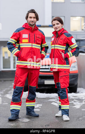 Lunghezza piena vista del personale paramedico in rosso uniforme in piedi con le mani nelle tasche Foto Stock