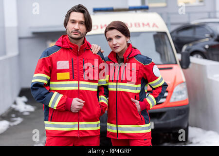 Stanco di personale paramedico in rosso uniforme in piedi di fronte a ambulanza Foto Stock