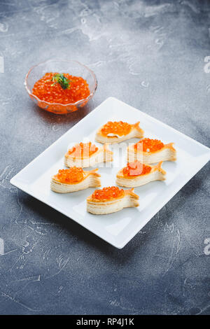 Deliziosa pasta sfoglia pasticcini a forma di pesce con caviale rosso su una tavola festiva. Foto Stock