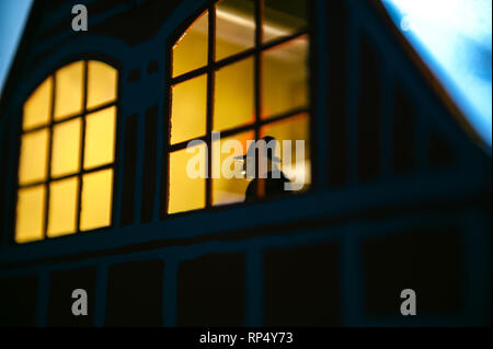 Casa giocattolo con windows illuminato dall'interno durante le vacanze di Natale e la figura di legno che appaiono nella finestra Foto Stock