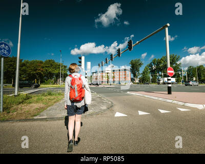 Vista posteriore della giovane donna che cammina su un incrocio nel centro di Haarlem, Paesi Bassi - strada che attraversa le luci Foto Stock