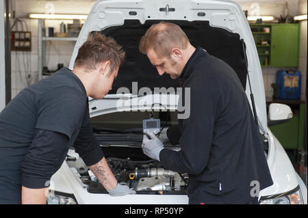 KFZ Teckniker Meister erklaert seinem Lehrling zum KFZ Mechatroniker wie eine Endoskop-Kamera funktioniert. In einer kleinen Werkstatt. [(C) Dirk A. F Foto Stock