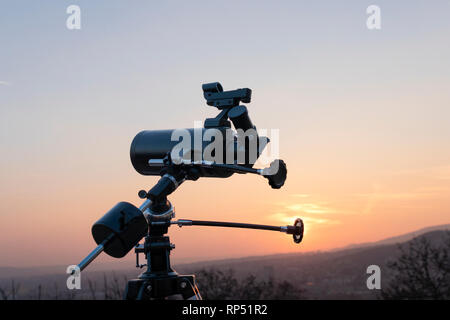 Un professionista di telescopio newtoniano montato su un treppiede, guardando una grande città al tramonto Foto Stock