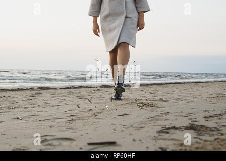 Carefree donna in pelle nera stivali kick sabbia sulla spiaggia. Battenti di sabbia umida. Concetto calzature di protezione, acqua e resistenza alla polvere. Foto Stock