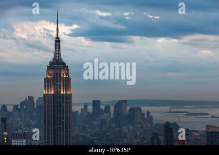 Crepuscolo dell'antenna vista del porto di New York, la statua della libertà su Ellis Island, edifici per uffici di Lower Manhattan con ingrandimento di lit top di impero Foto Stock