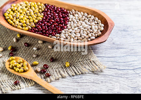 Varietà di Fagioli sul cucchiaio di legno su sfondo di legno. fagioli, arachidi, fagioli rossi e fagioli marrone. Foto Stock