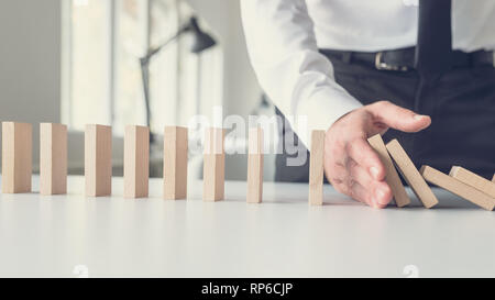 Attività di gestione delle crisi - il concetto di mediatore di affari arrestando la caduta dei dominos con la sua mano. Foto Stock